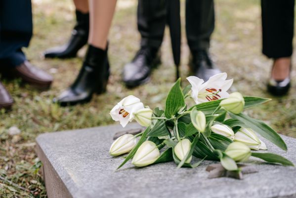 White lilies laid on a gravestone surrounded by people in mourning attire outdoors.