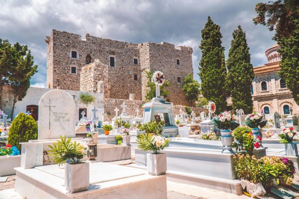Vibrant Greek cemetery in Samos showcases historic architecture, surrounded by lush greenery and gravestones under a dramatic sky.