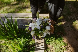A man places a bouquet of flowers on a grave in a peaceful cemetery setting.